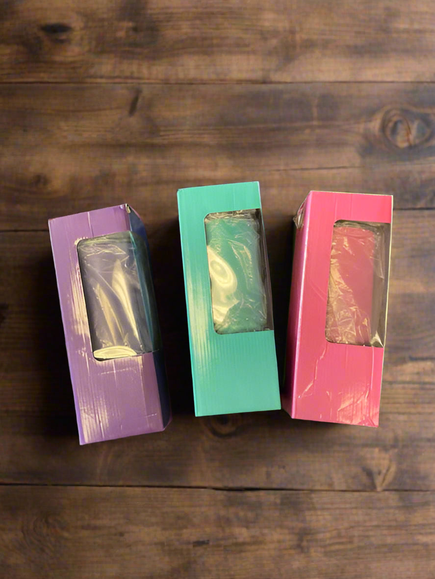 Three packaged tumblers in pastel-colored boxes—purple, teal, and pink—standing upright on a rustic wooden surface. Each box features a clear plastic window, showcasing the tumbler inside, making them perfect for custom-engraved or personalized drinkware gifts