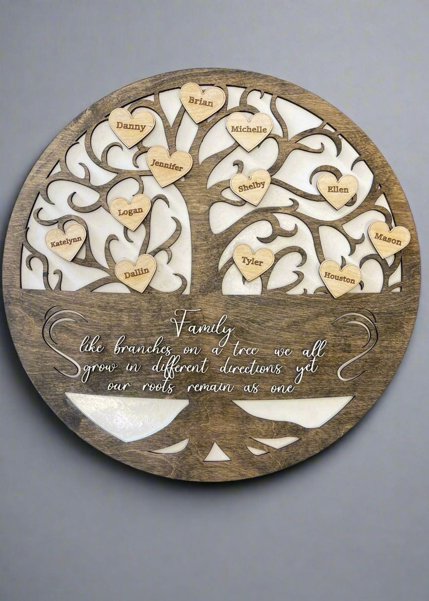 A circular wooden family tree plaque with intricately carved branches and heart-shaped name tags. The names on the hearts include Brian, Michelle, Danny, Jennifer, Logan, Katelyn, Dallin, Shelby, Ellen, Tyler, Mason, and Houston. Below the tree, an engraved quote reads: "Family, like branches on a tree we all grow in different directions yet our roots remain as one." The background is a soft white material, contrasting with the dark wood.