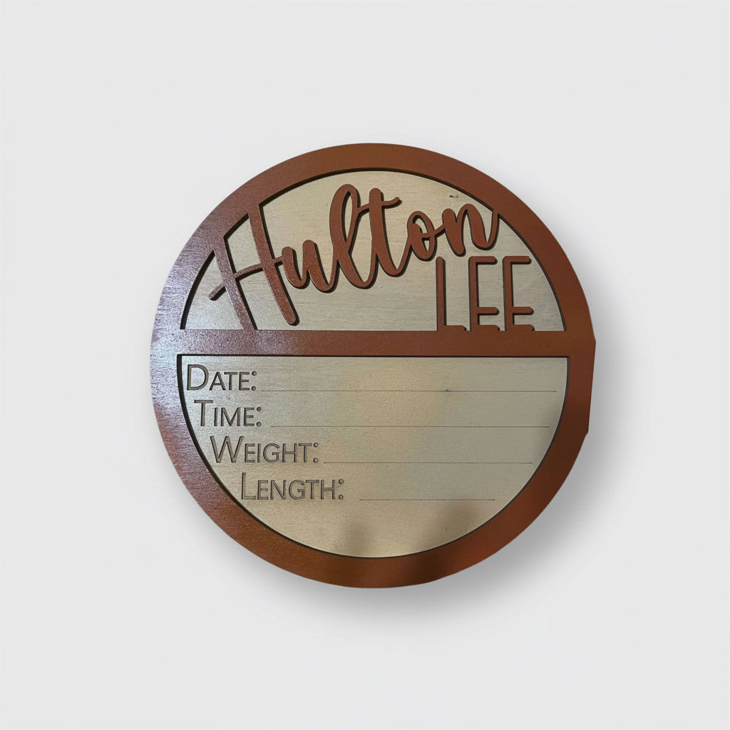 Personalized round wooden baby name announcement sign with birth details on a light pink background