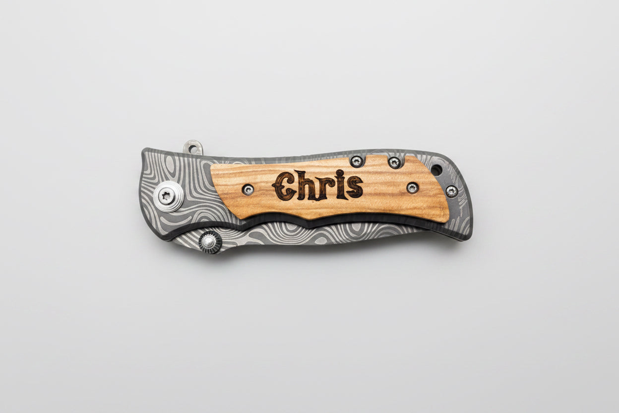 Custom Damascus pocket knife with wood handle engraved 'Chris' on wood table.