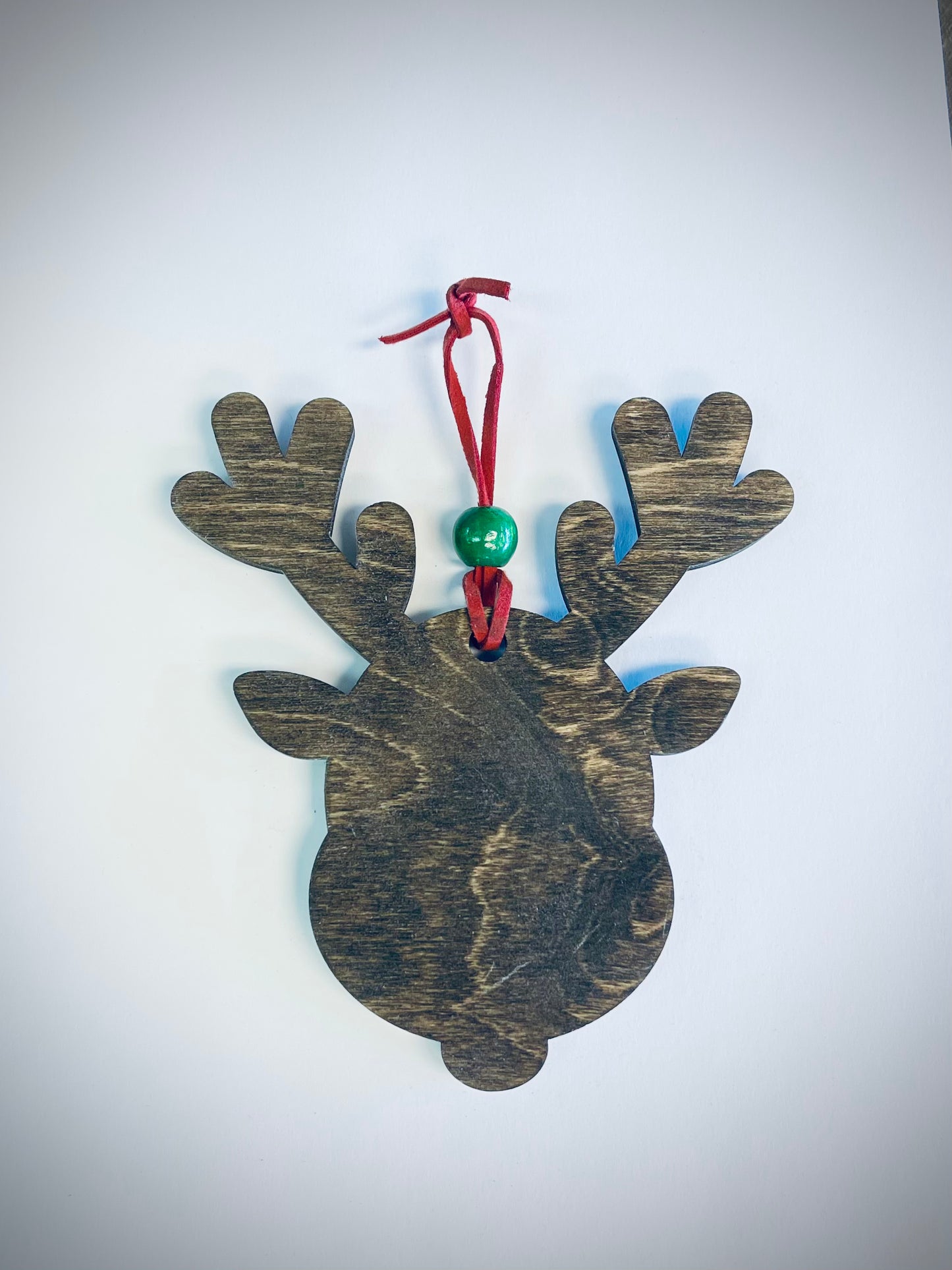 Wooden reindeer ornament with antlers, green bead, and red string on white background
