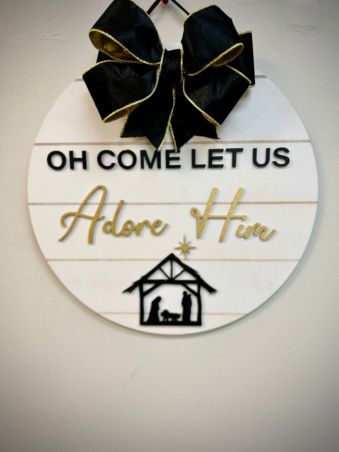 Round Christmas door hanger with 'Oh Come Let Us Adore Him' text, black bow, nativity scene.