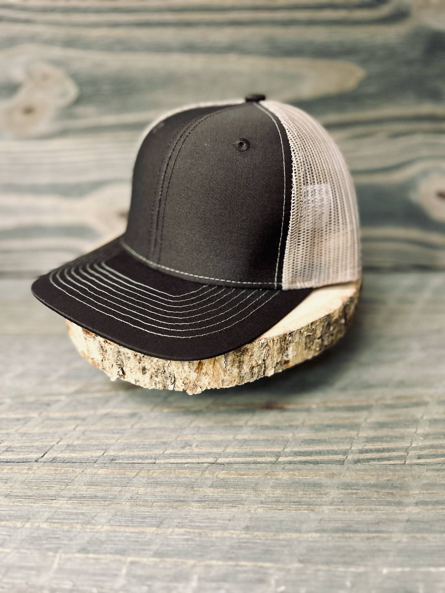Black Richardson trucker hat with mesh back on wood slice, rustic wood background