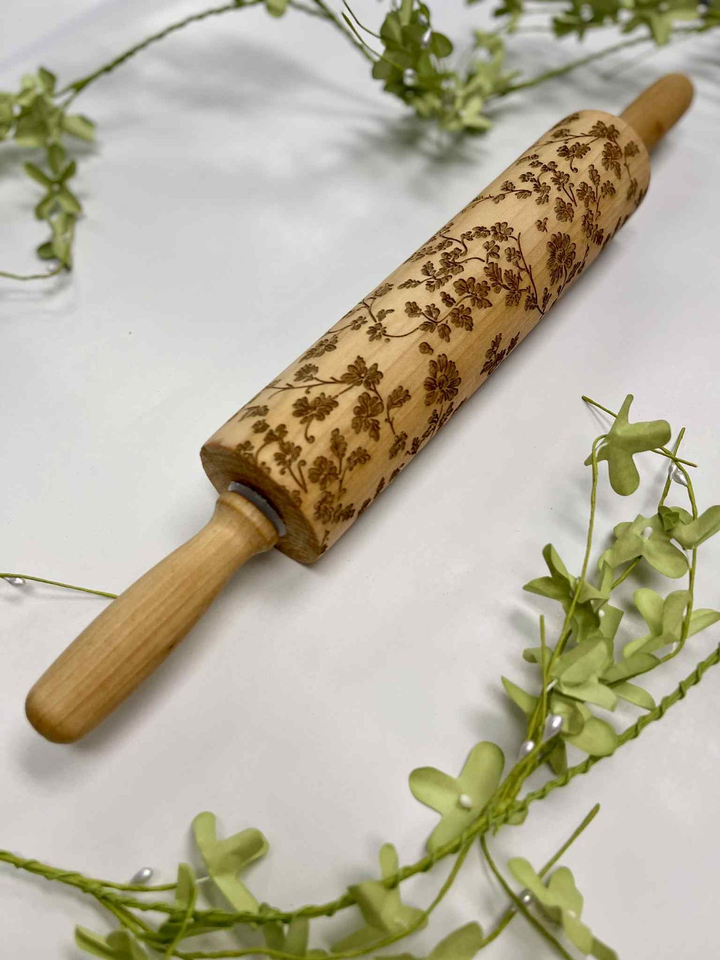 Engraved wooden rolling pin with floral pattern on white background and green foliage