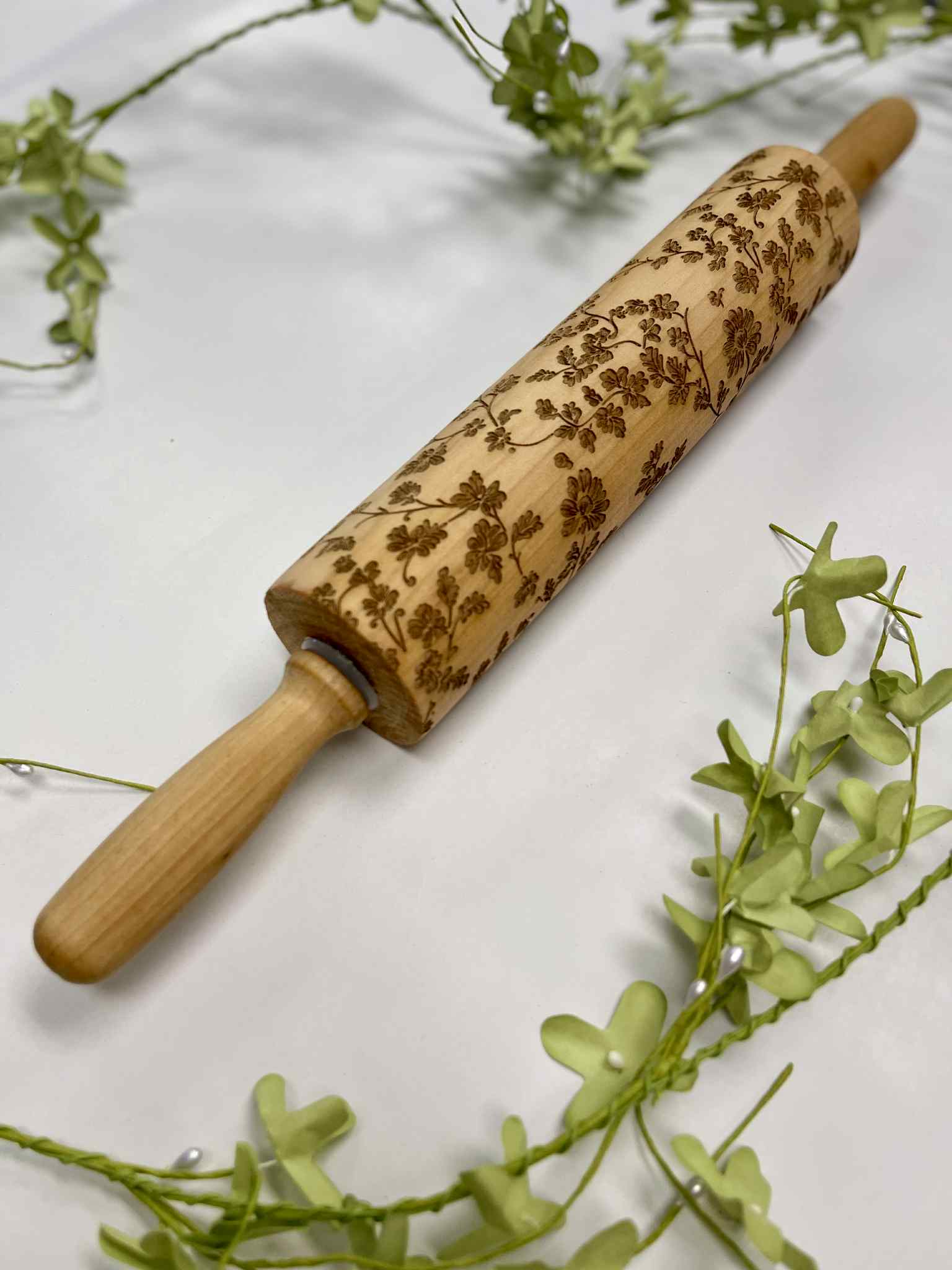 Engraved wooden rolling pin with floral pattern on white background and green foliage