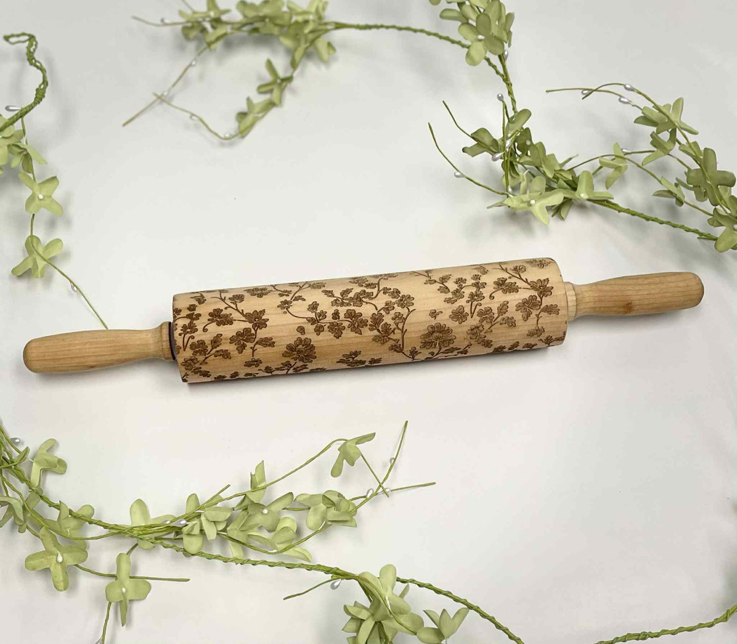 Laser-engraved wooden rolling pin with floral pattern on white background and green vines