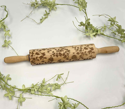 Laser-engraved wooden rolling pin with floral pattern on white background and green vines