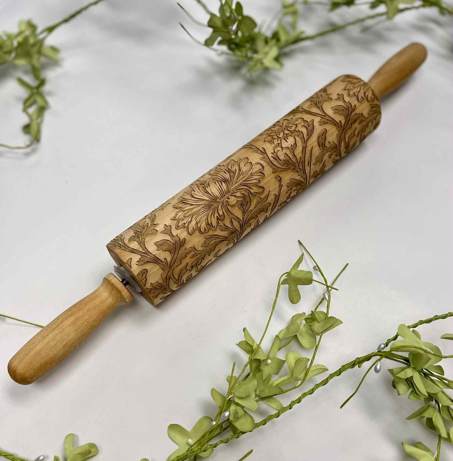 Engraved wooden rolling pin with floral design on white surface and green leaves