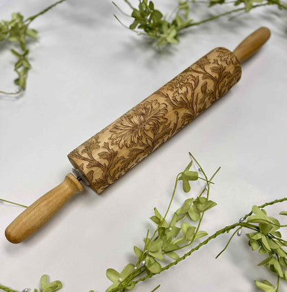Engraved wooden rolling pin with floral design on white surface and green leaves