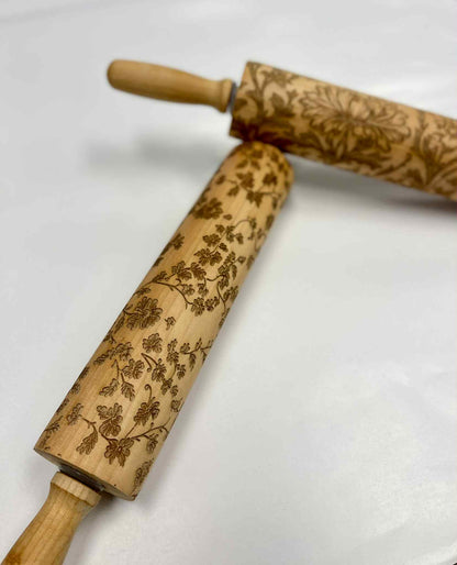Two embossed wooden rolling pins with floral patterns on a white background