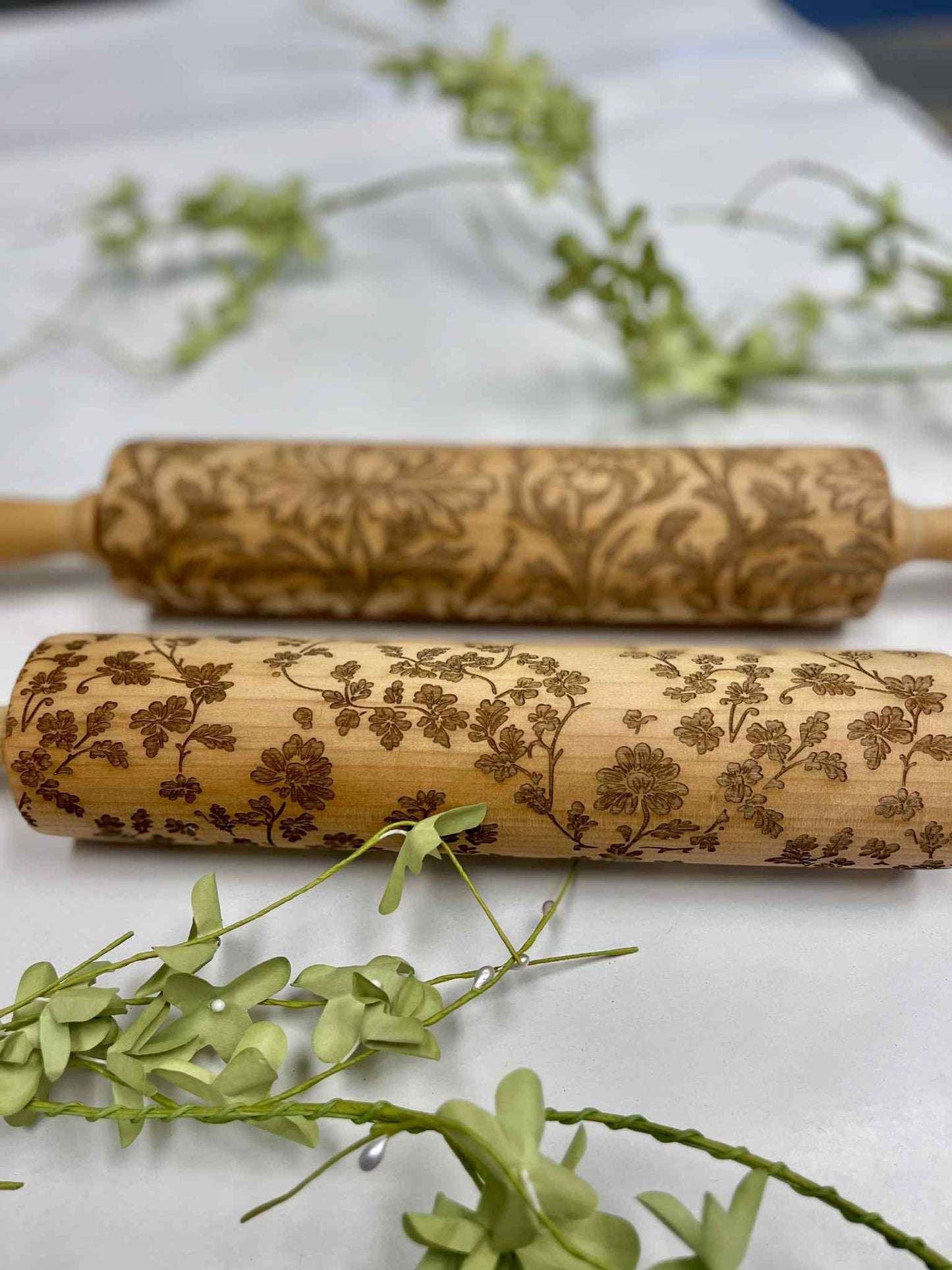 Decorative wooden rolling pins with floral engravings on white surface with green leaves
