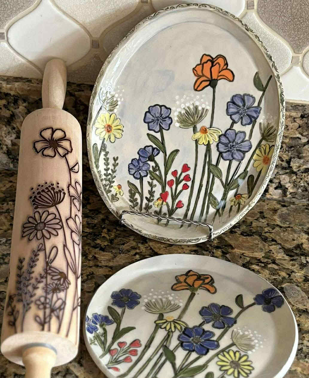 Floral rolling pin and ceramic plates with hand-painted wildflower designs on granite countertop