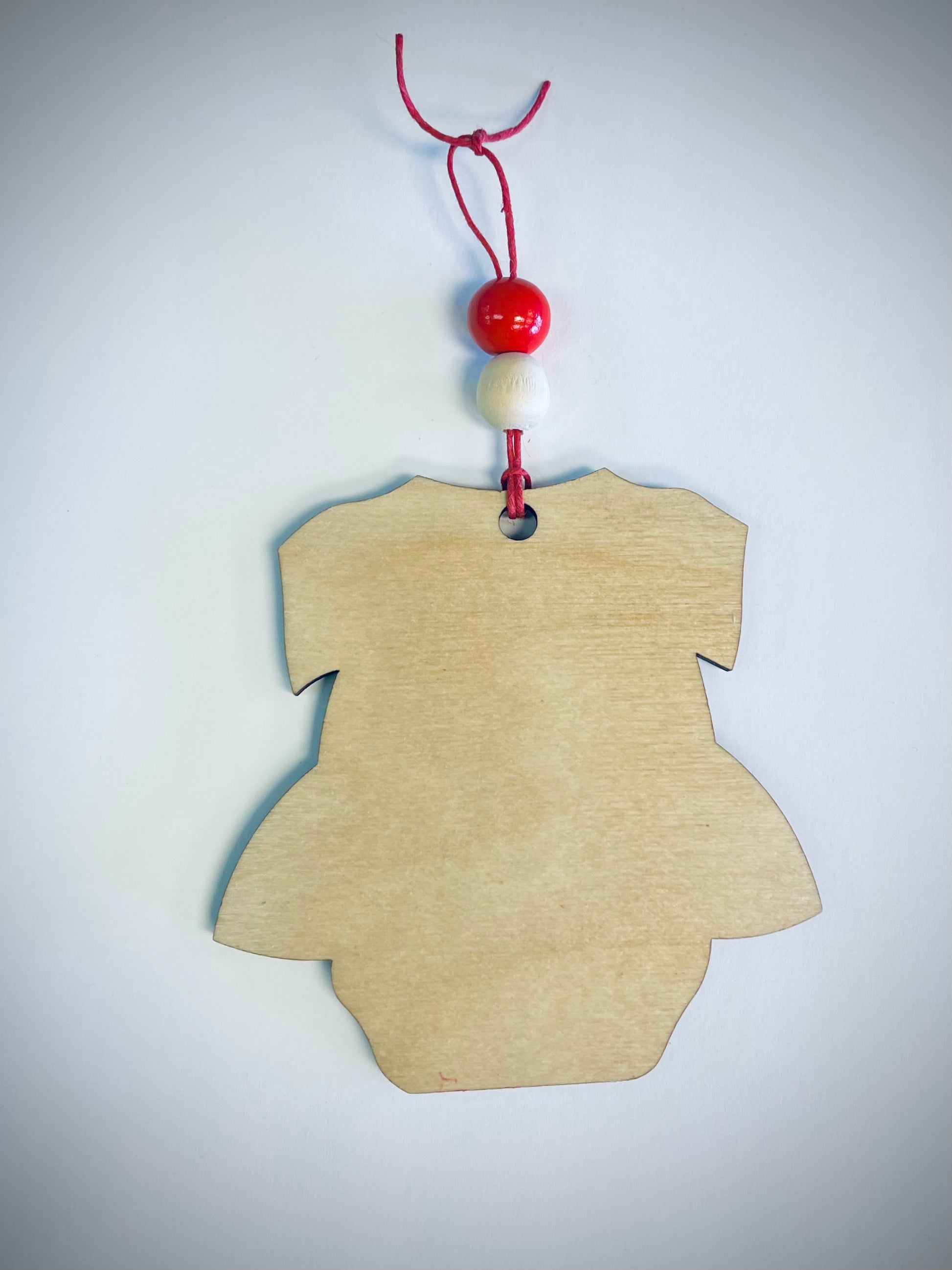 Wooden onesie ornament with red and white beads on red string, plain white background