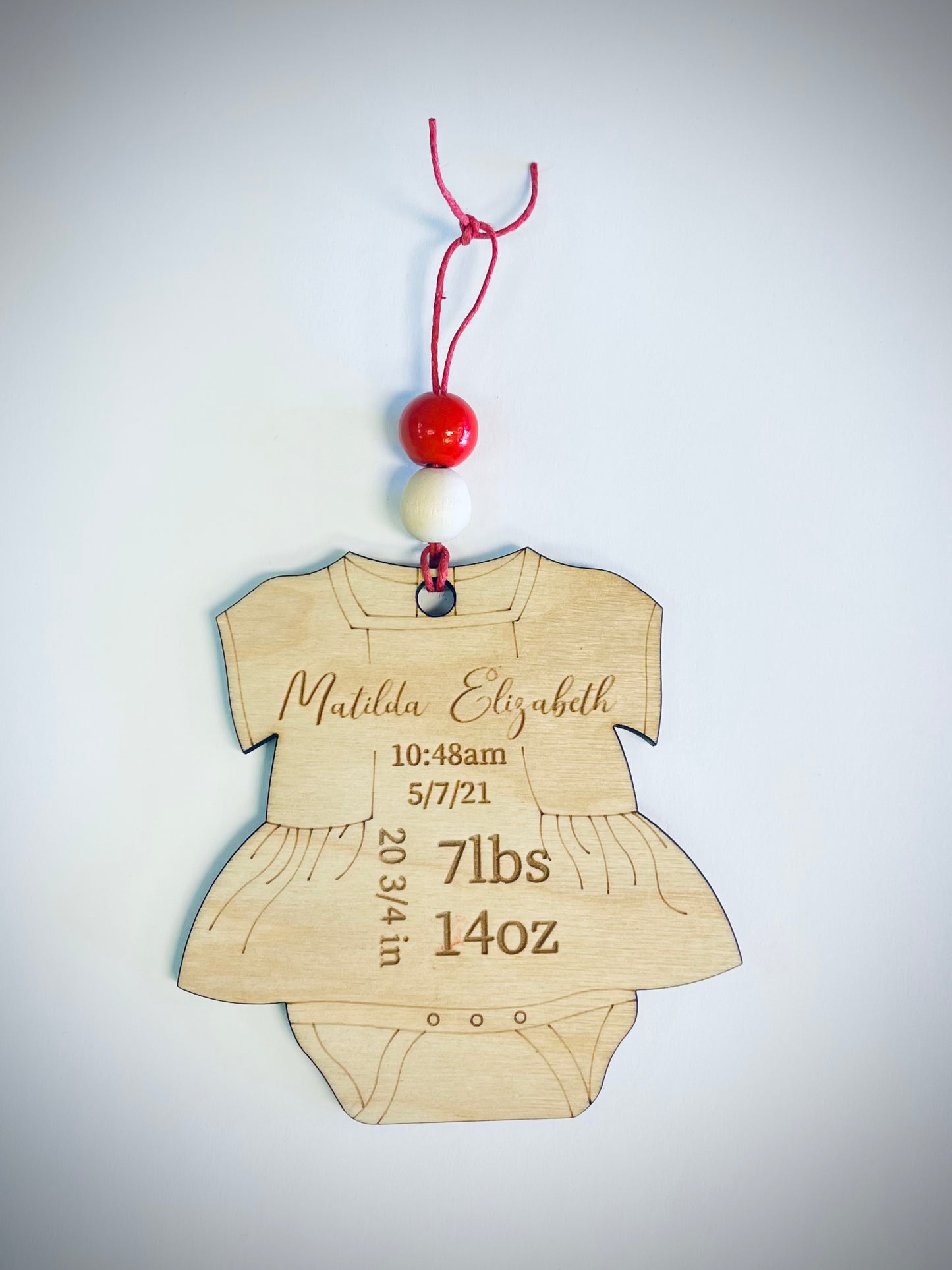 Wooden baby onesie ornament with red and white beads, personalized birth details engraved