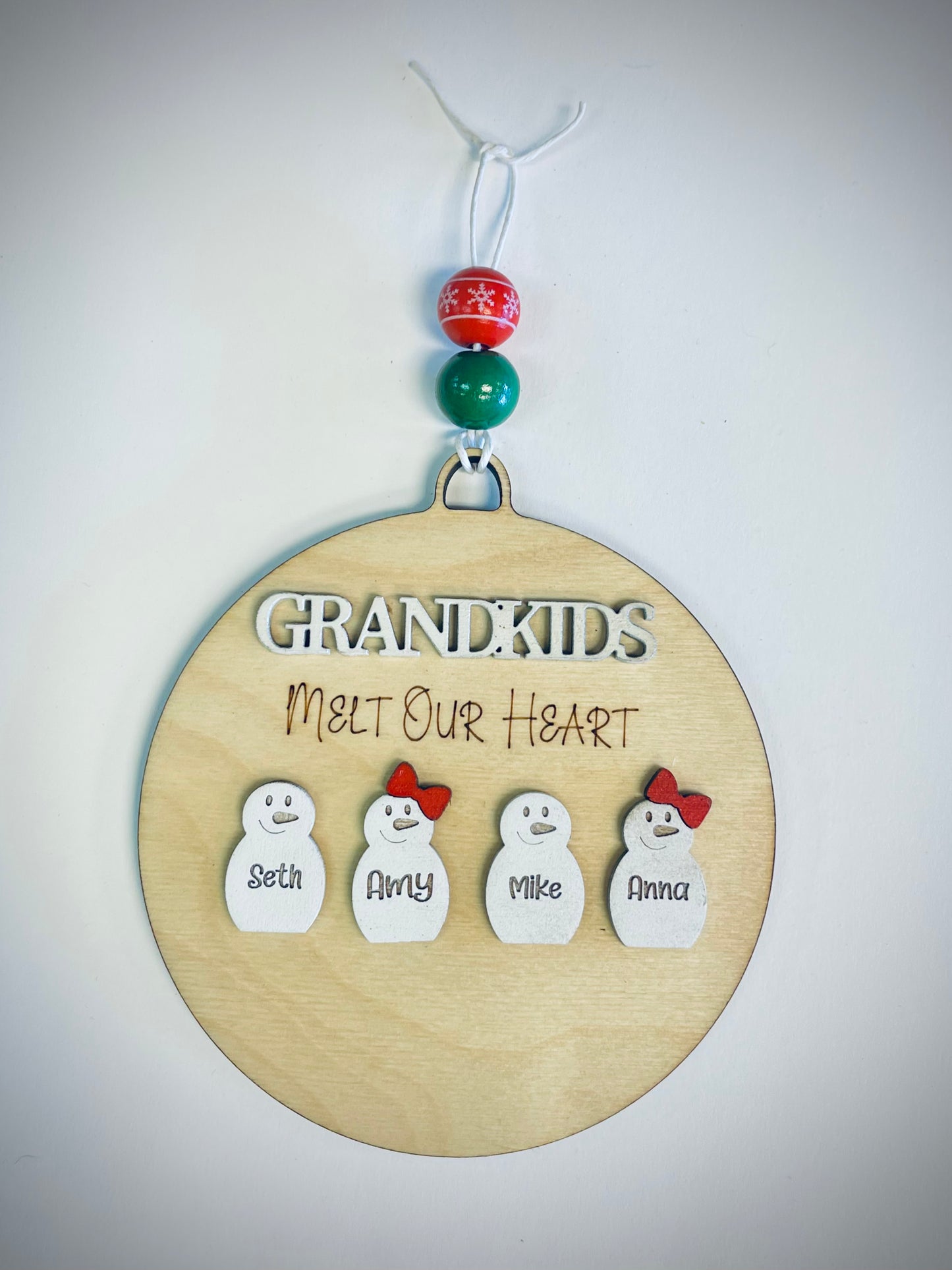 Wooden ornament with 'Grandkids Melt Our Heart' text and four snowmen with names, festive beads