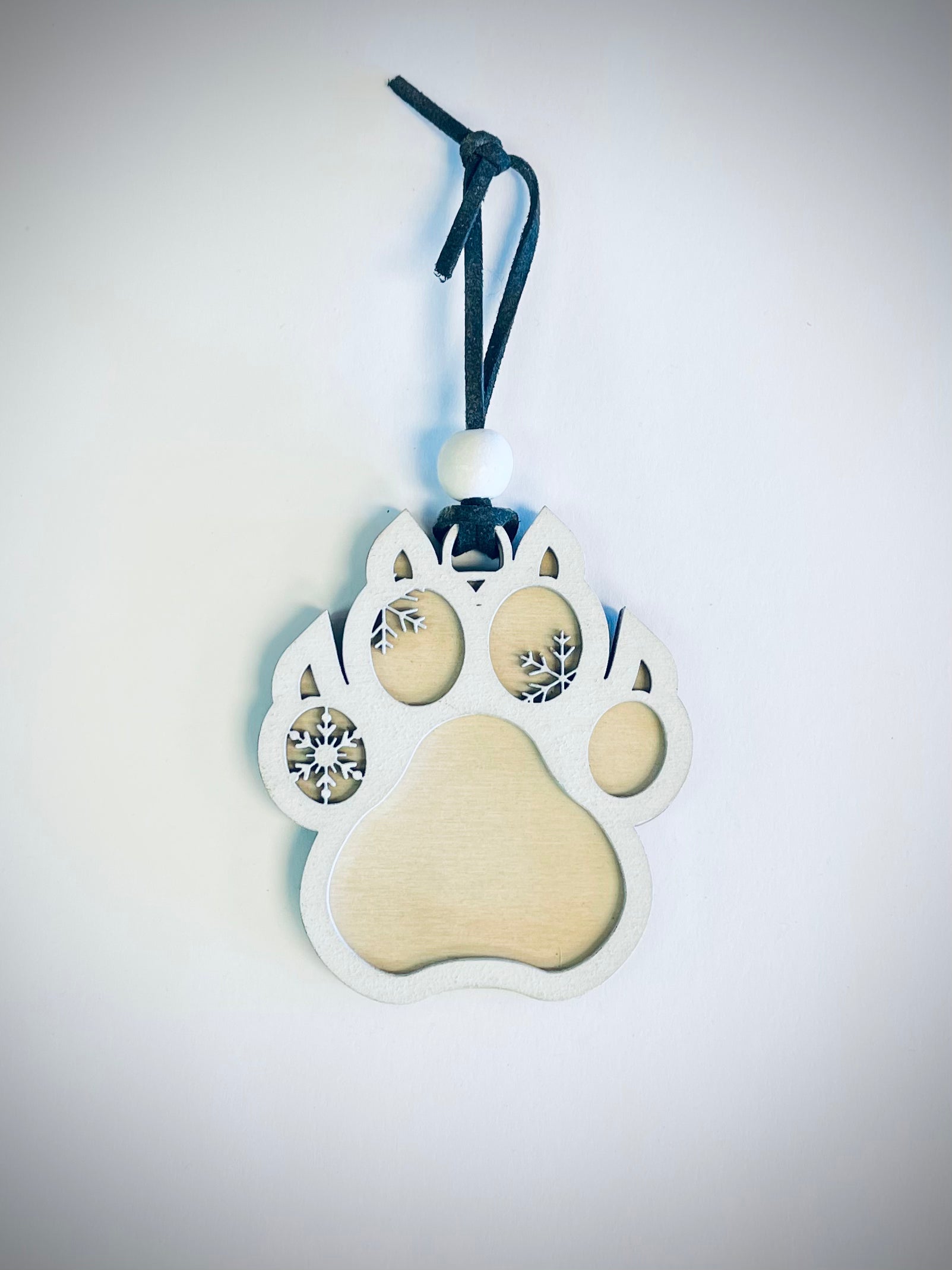 Wooden cat paw ornament with snowflake cutouts and black string on white background