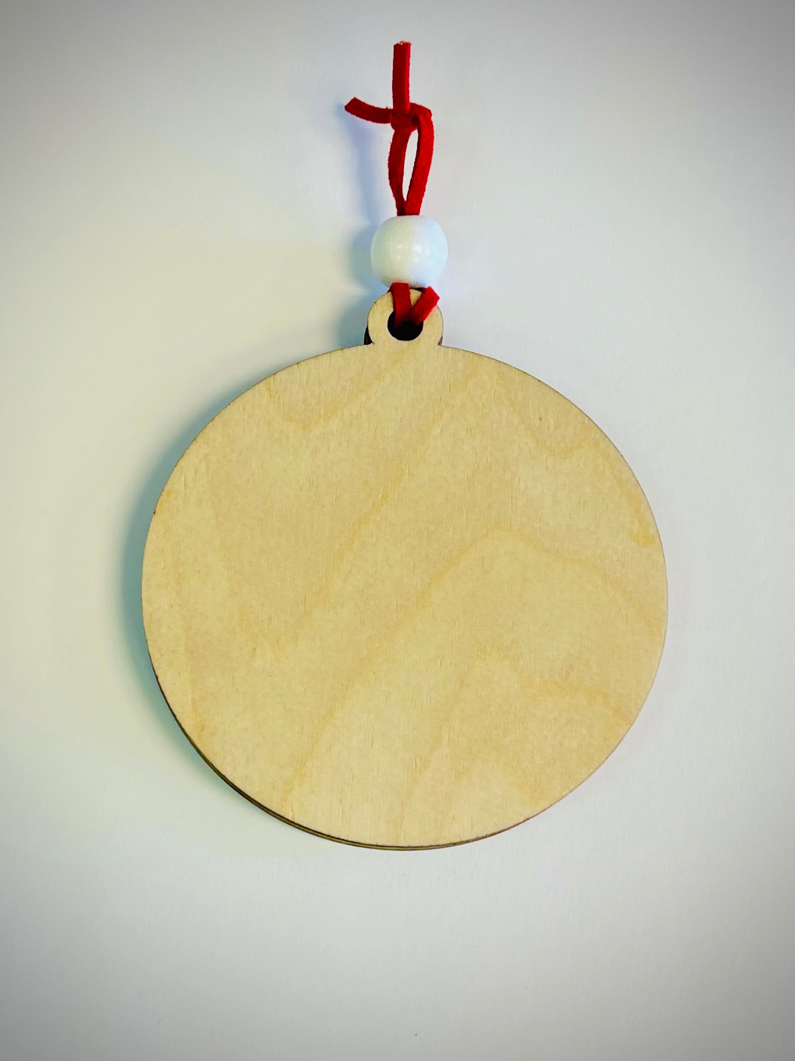 Blank round wood ornament with red string and white bead on white background