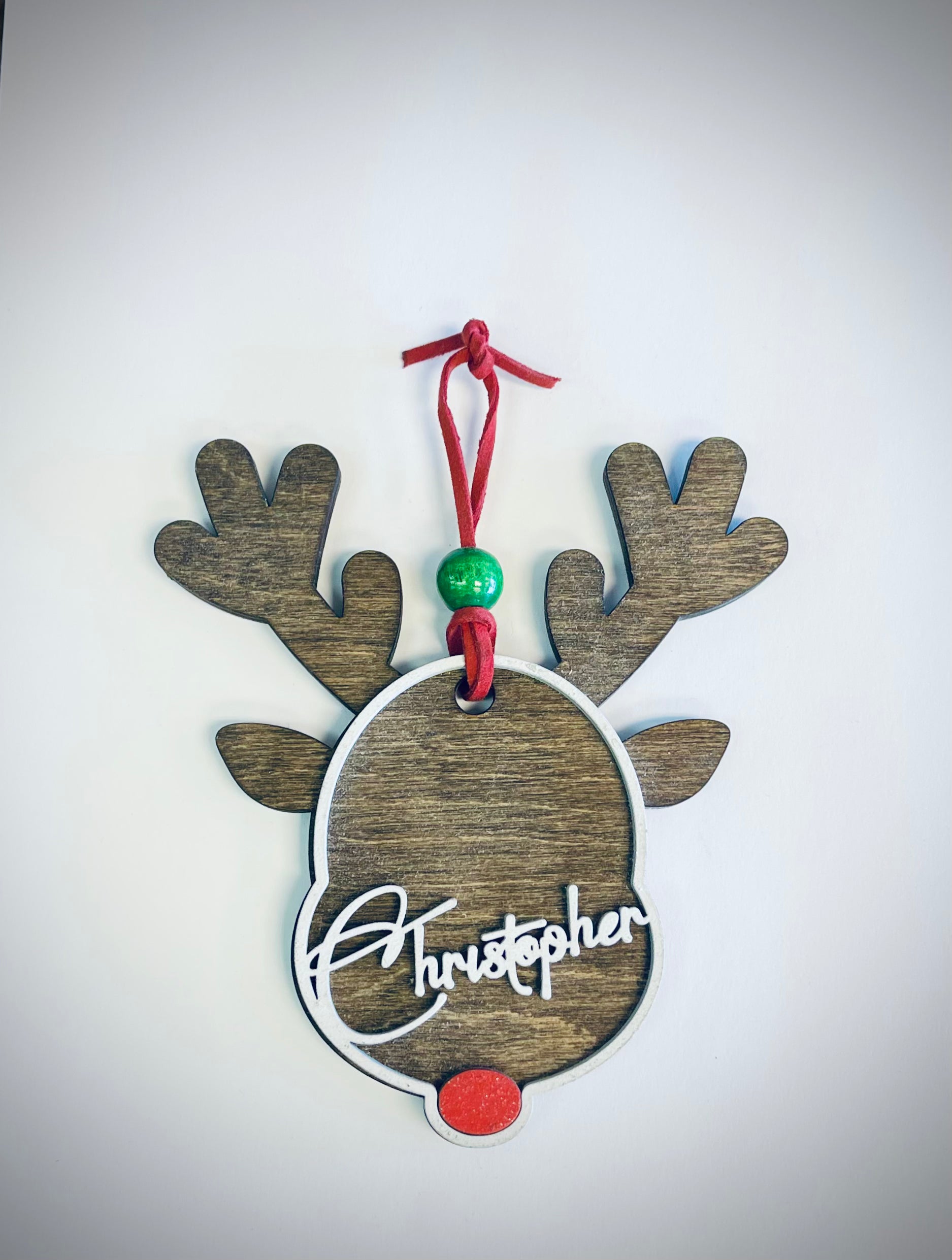 Personalized wooden reindeer ornament with antlers, red nose, and green bead on white background