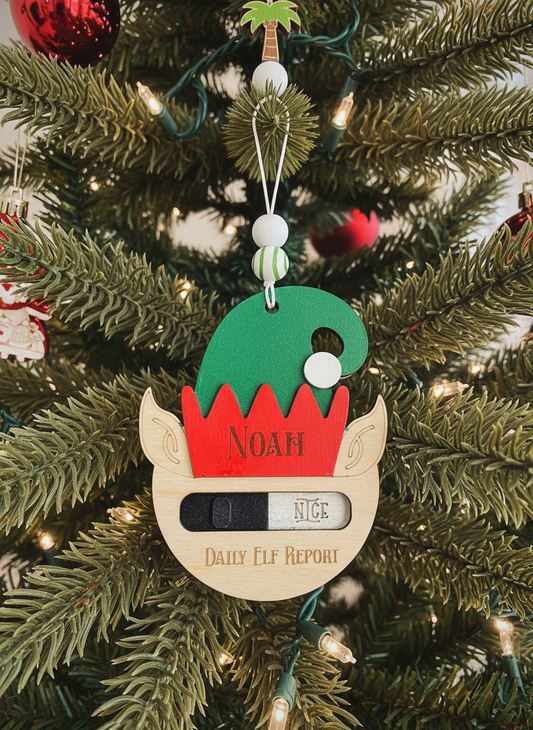 Elf ornament with green hat, red trim, and 'Noah' on Christmas tree, Daily Elf Report slider on 'Nice'.