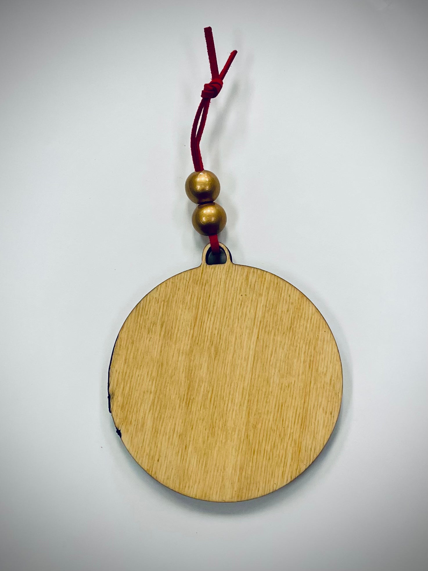 Round wooden ornament with gold beads and red cord on white background