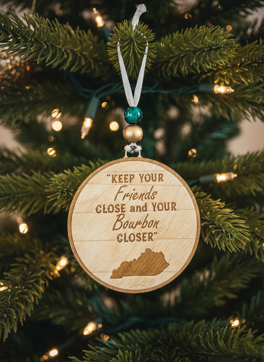 Wooden bourbon-themed Christmas ornament on tree, engraved with 'Keep your friends close and your bourbon closer'.