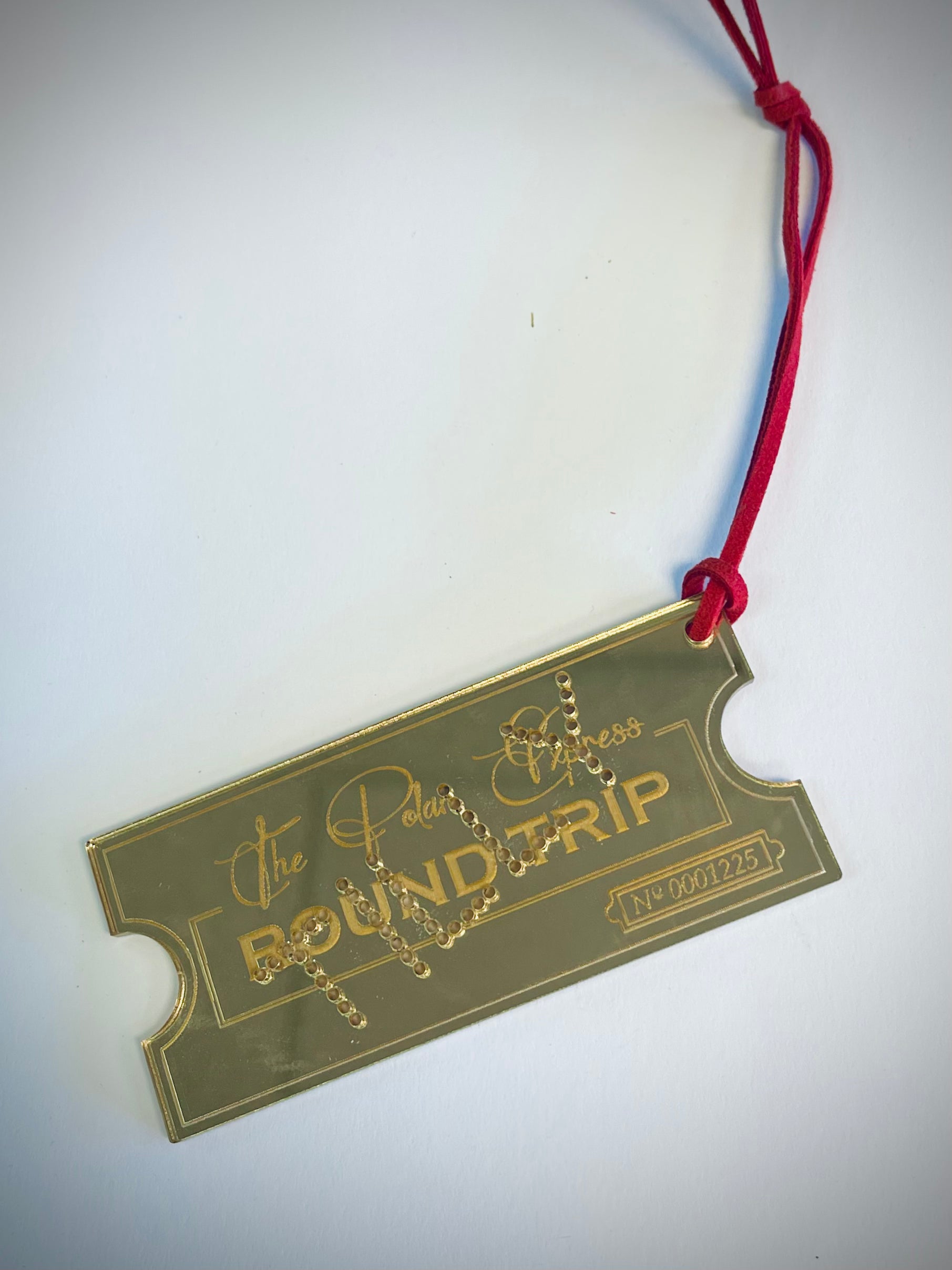 Polar Express ticket ornament with gold finish and red string on white background