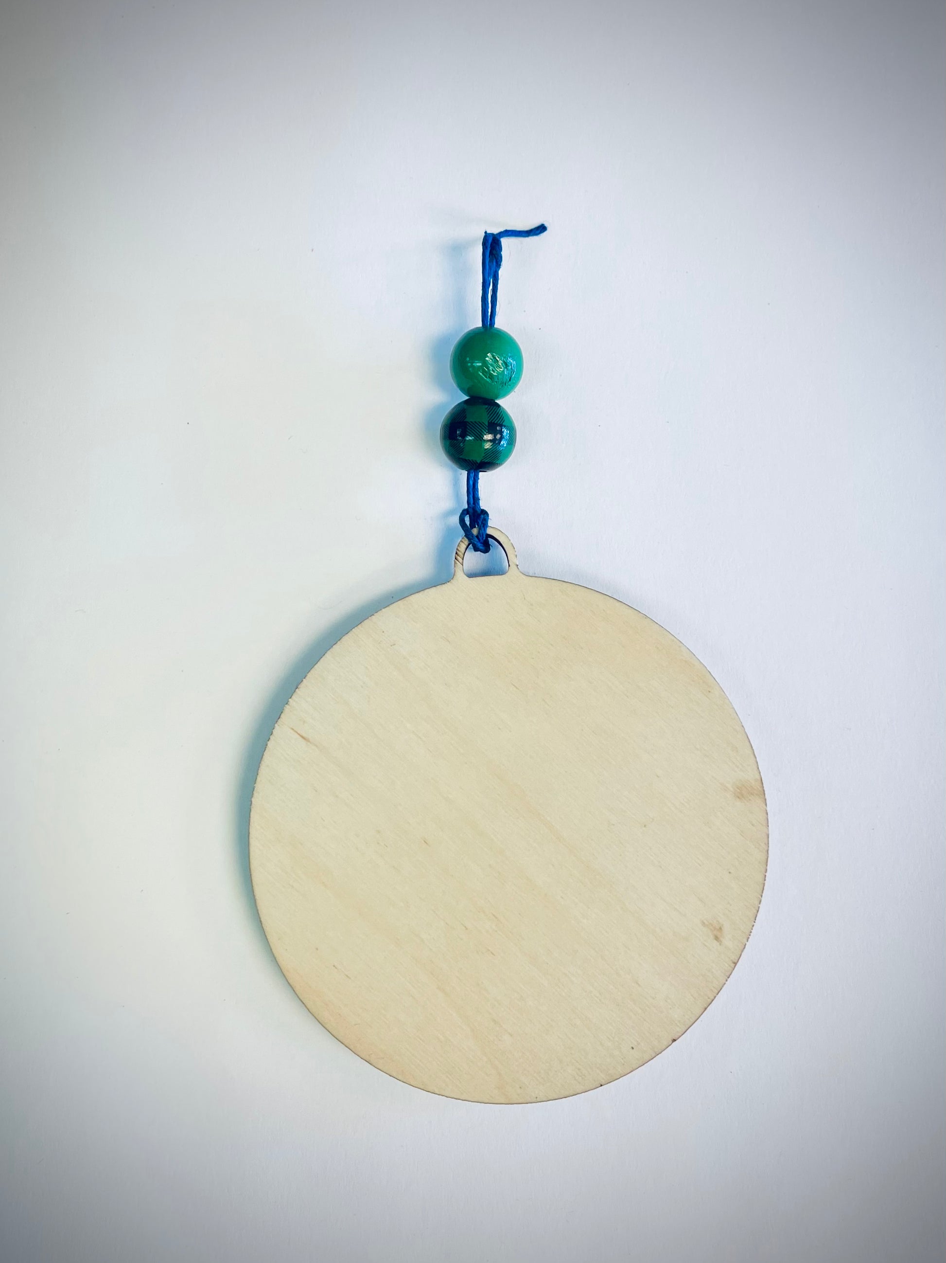 Round wood ornament with blue string and two green beads on white background