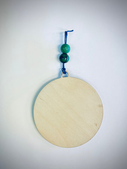 Round wood ornament with blue string and two green beads on white background