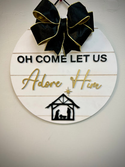 Round Christmas door hanger with 'Oh Come Let Us Adore Him' text, black bow, nativity scene.