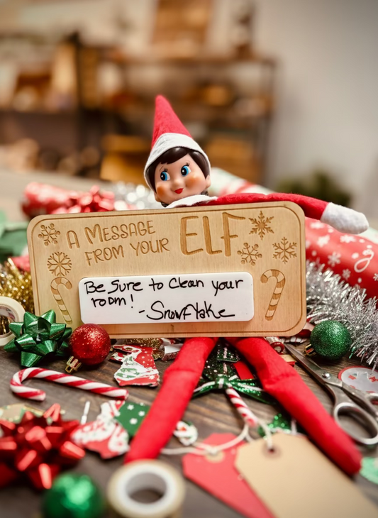 Elf on the Shelf with Christmas message board, surrounded by festive decorations