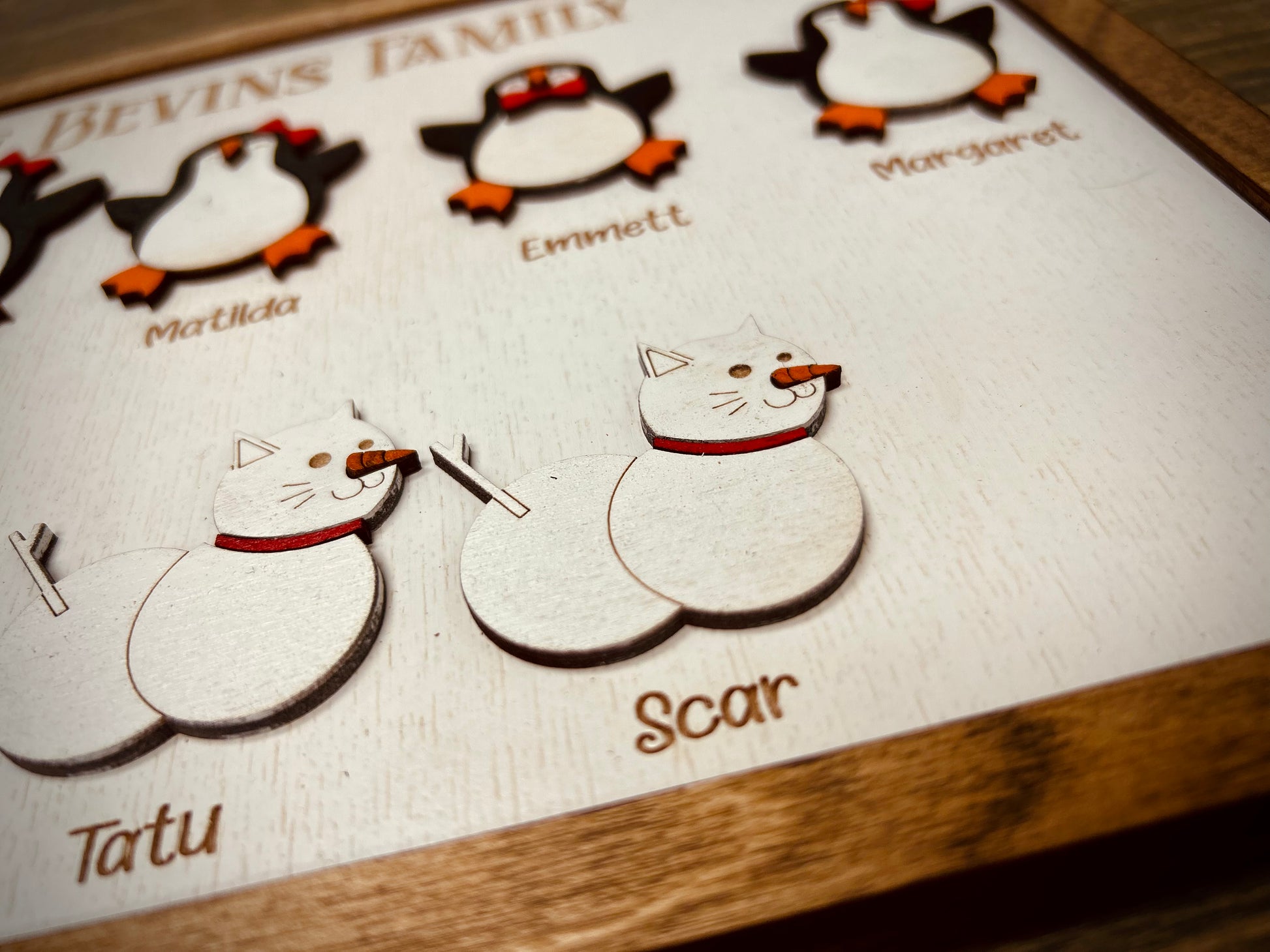 Wooden family plaque with cartoon penguins and snow cats, names engraved below each figure