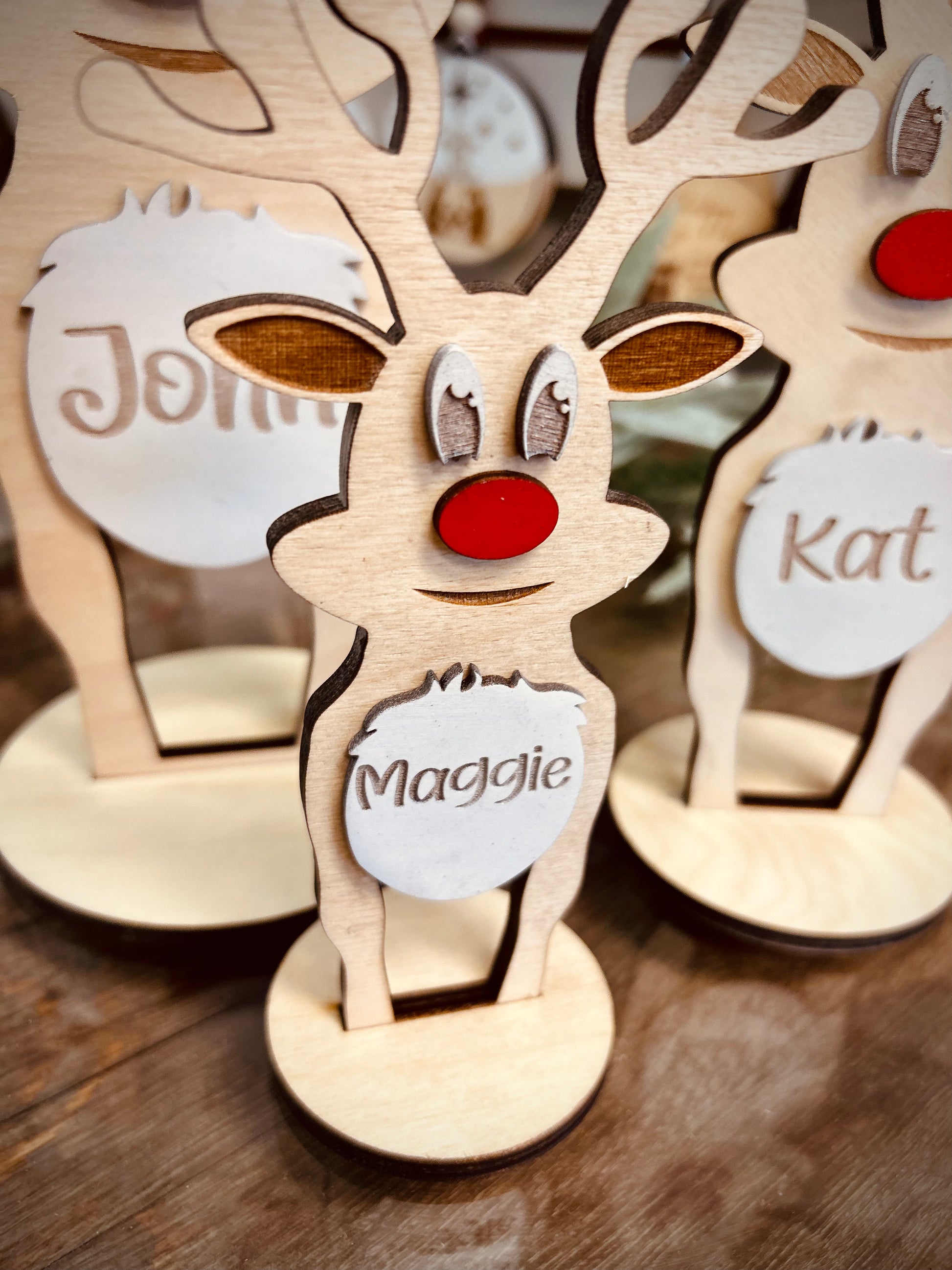 Personalized wooden reindeer Christmas decorations with red noses on a table.