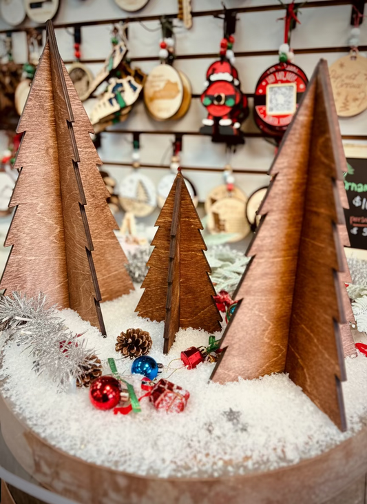 Wooden Christmas trees on fake snow with ornaments, pine cones, and festive holiday decor.